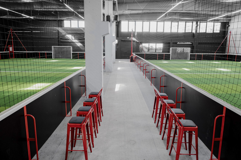 Allée bordée de tabourets rouges entre deux terrains de foot indoor