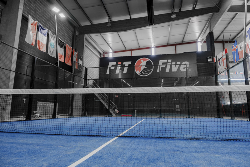 Court de padel intérieur au sol bleu avec filet et vitrage